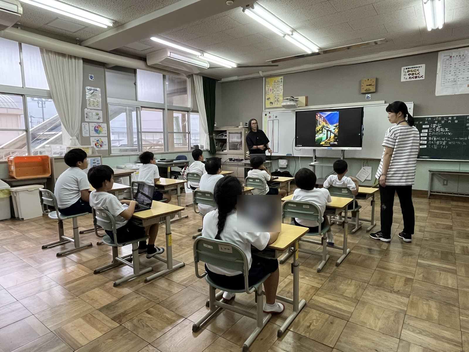 窓側から見た授業の様子。講師とアシスタントが前に立ち、児童が座って話を聞いている